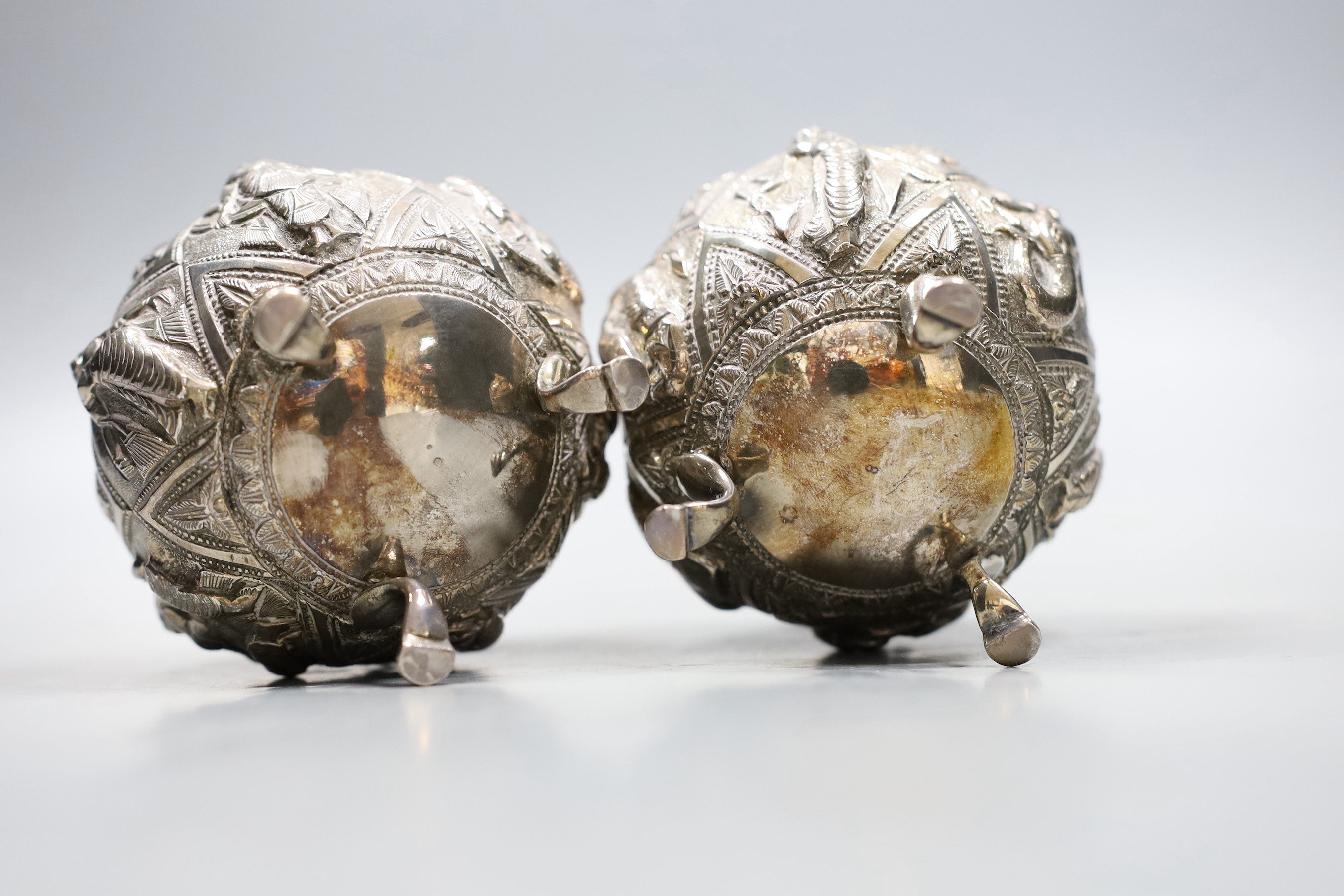 A pair of Indian embossed white metal circular bowls, on three hoof feet, height 82mm.